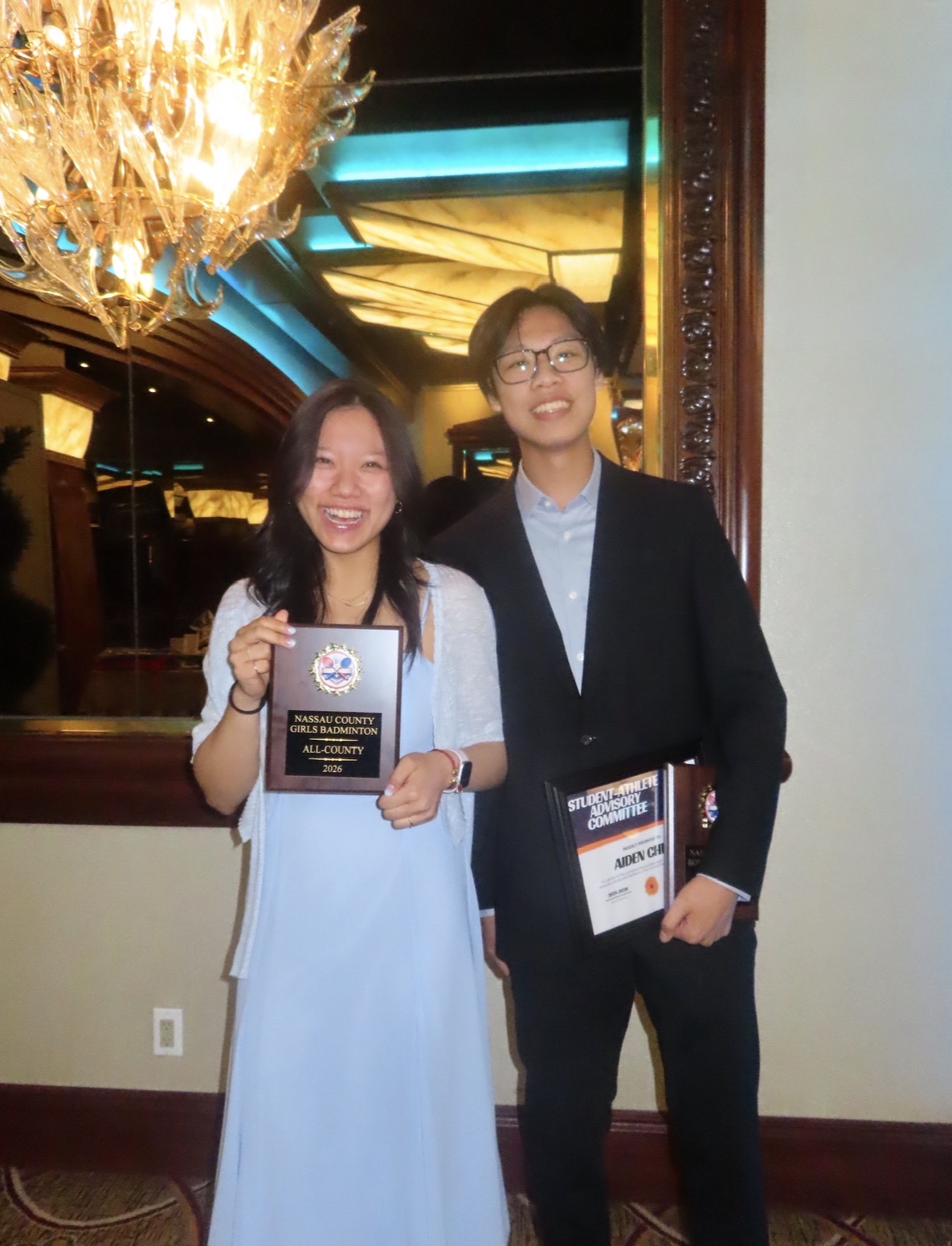 Sandra and a friend at a badminton awards event, holding a Nassau County All-County plaque